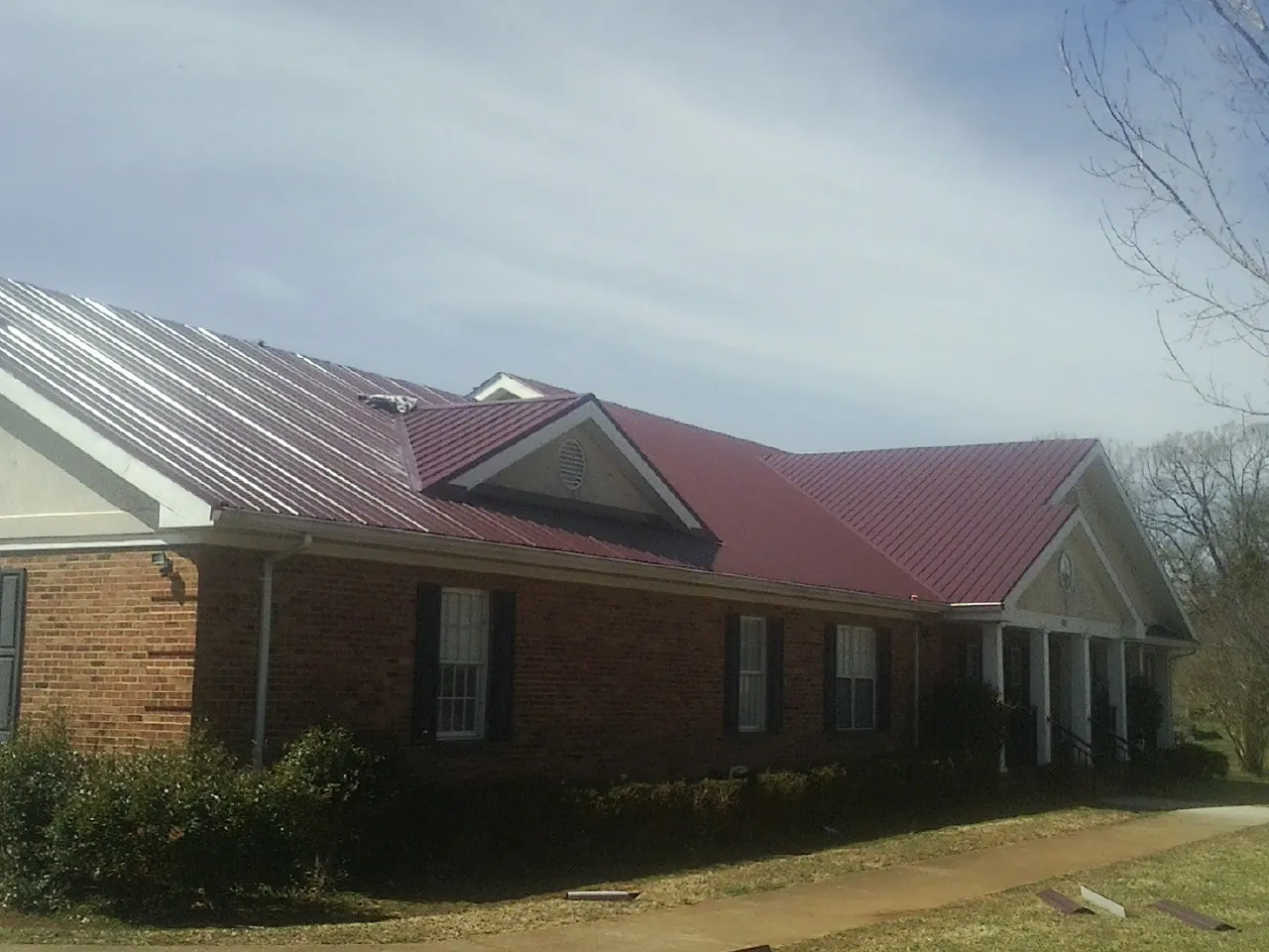 Red metal roof with gabled entries on a long brick building, from a Hail Damage Roof Repair job in Ohio City