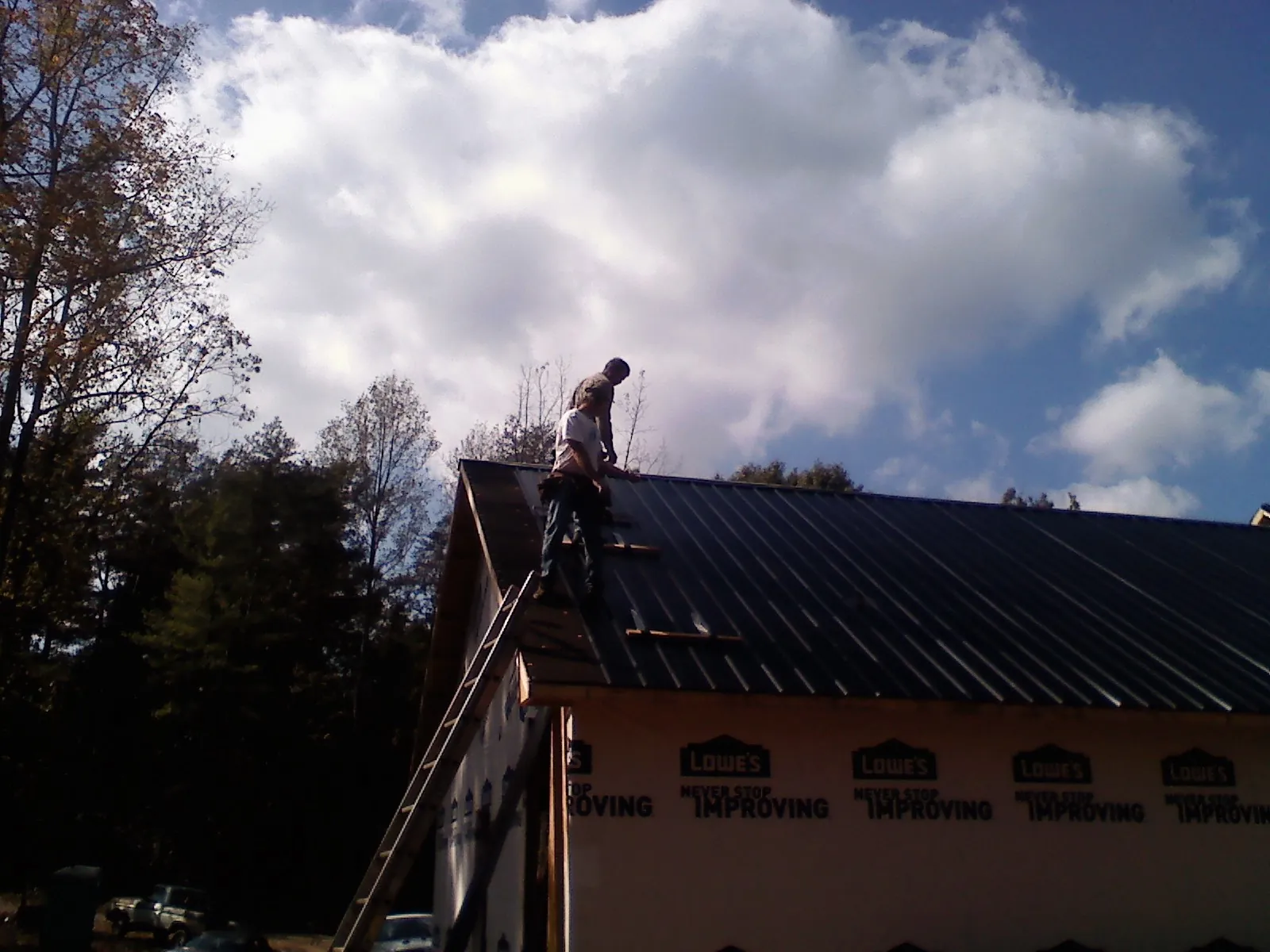 Roofer fastening dark metal panels high against a cloudy sky, from a Roof Inspection job in Ohio City