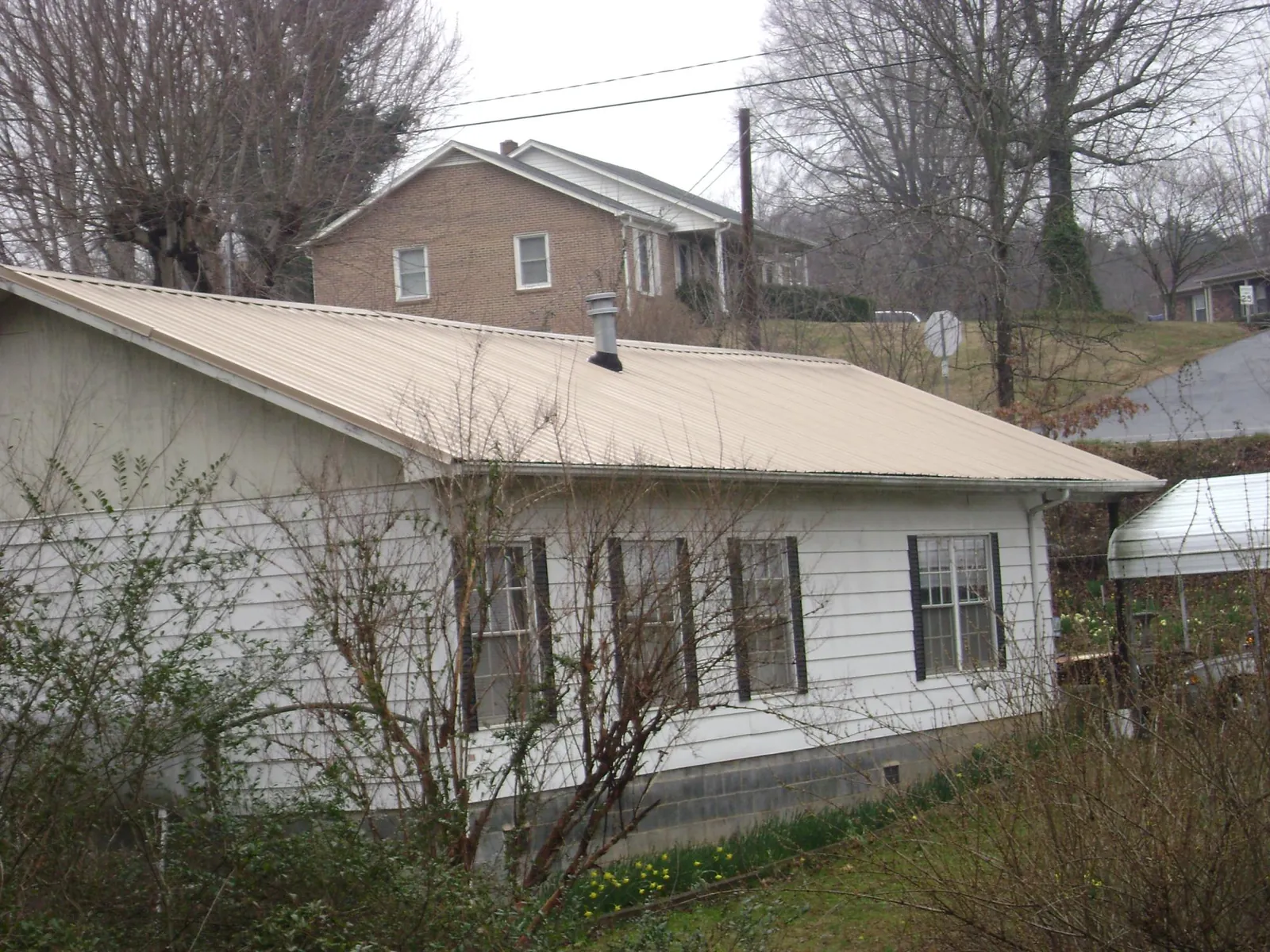 Tan metal roof on a white sided house set into a hillside — Commercial Roofing by Roofing Brothers in Ohio City
